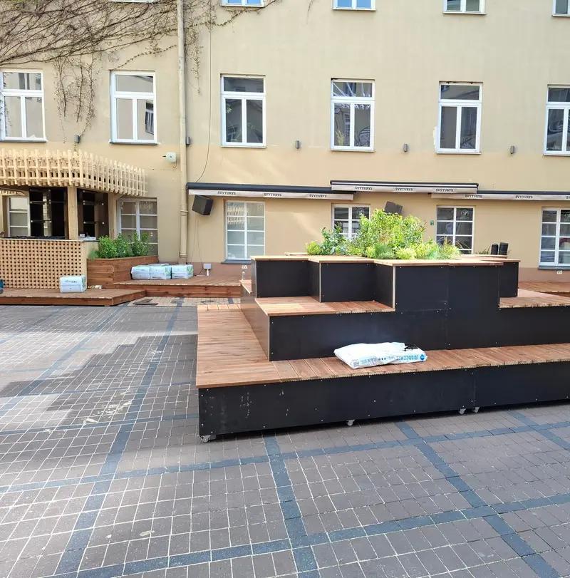 Pakopinės sėdimos vietos su medinėmis lentelėmis ir gėlinėmis viršuje, fone terasų platformos