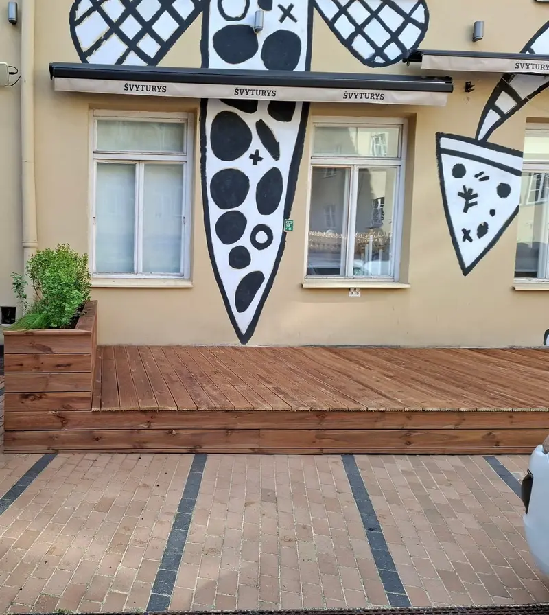 Medinė terasos platforma prie pastato fasado, jos gale medinė gėlinė