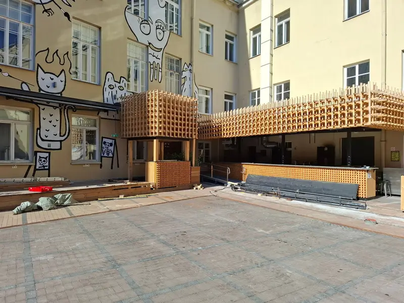 Kioskas su medinių grotelių kubu ant stogo ir ilgas baras kieme