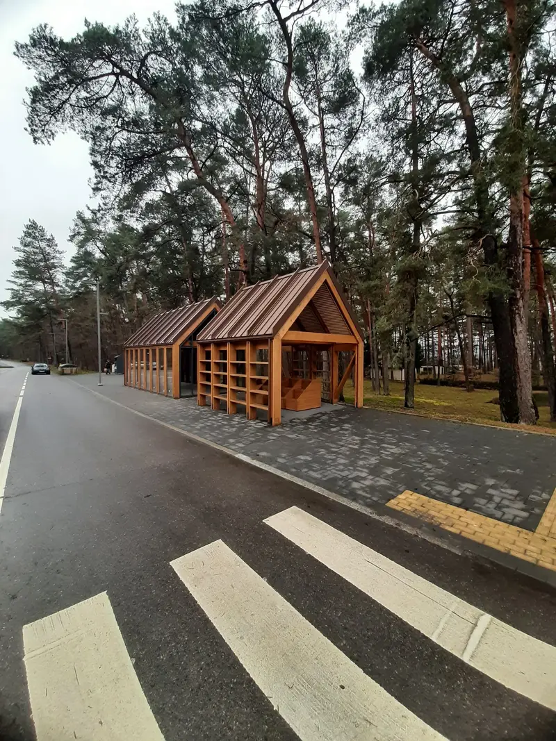 Atviro paviljono galas su dvišlaičiu stogu ir įstiklintas paviljonas už jo, žiūrint nuo perėjos