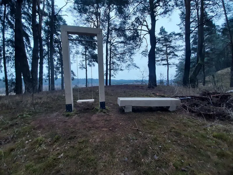 Medinis sūpynių rėmas su ant grandinių pakabinta sėdyne ir masyvus suolas pušyne